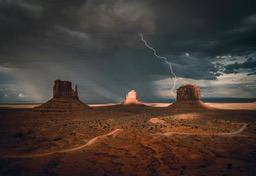 A magnificent scene before a storm, lightning strikes across a cloudy sky, illuminating the distant rock pillars and the desolate desert. - free wallpaper image