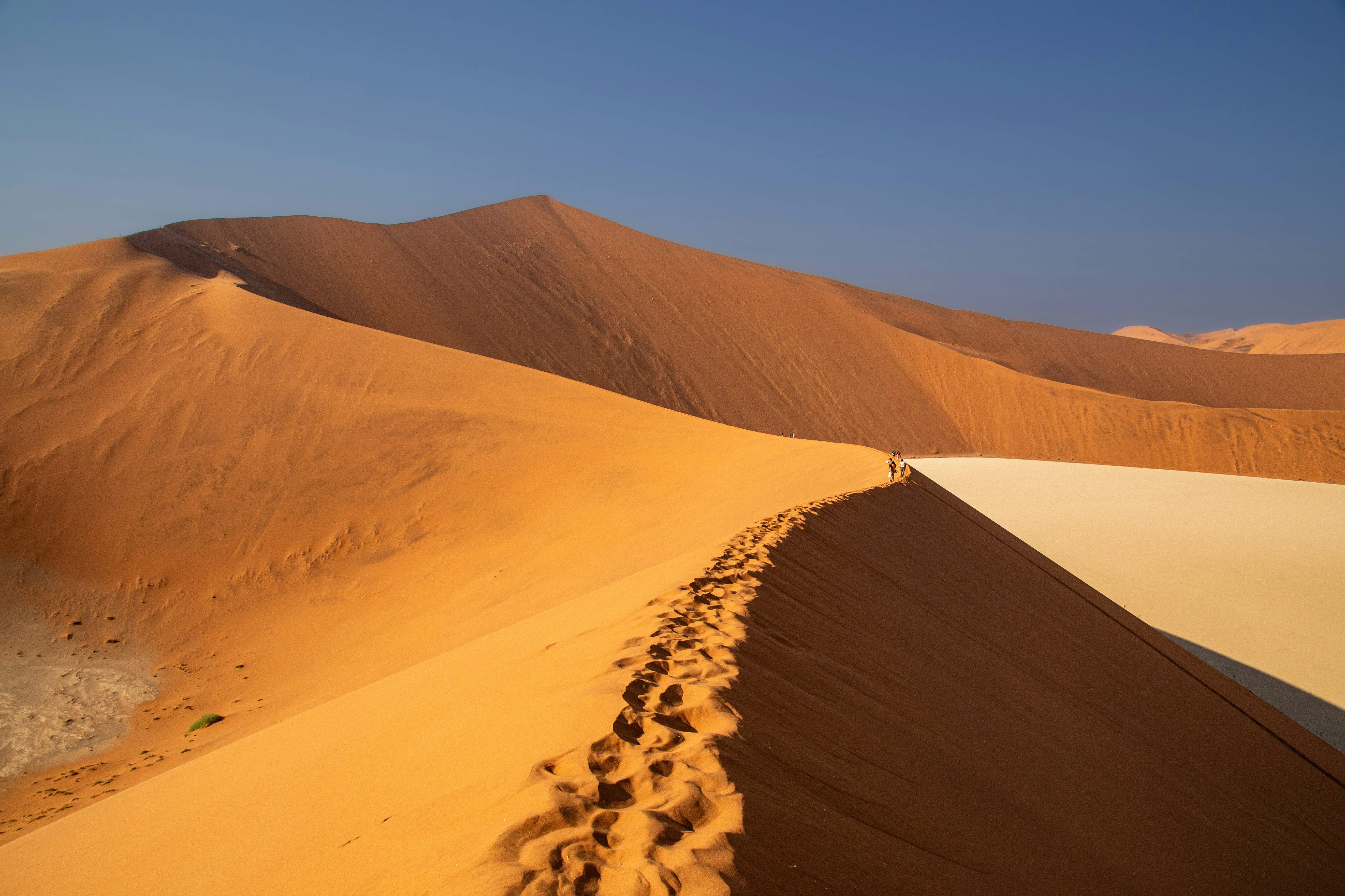 A group of people are walking on a winding sand dune in the desert, the sand dune is golden yellow and the sky in the distance is azure. - free wallpaper image