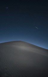 A starry night sky with a shooting star, a sand dune stands silently in the desert. - free wallpaper image