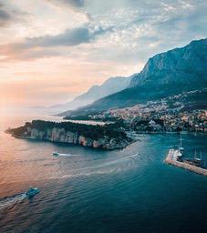 At dusk, the sun shines on the coastline, the mountains in the distance are shrouded in clouds, a city is built on the mountain, and there are several ships sailing on the sea. - free wallpaper image