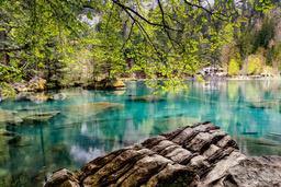 The lake is a beautiful emerald green color, the water is clear and you can see the bottom, surrounded by lush trees and rocks. - free wallpaper image