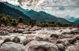 A fast-flowing river in the mountains, the riverbed is covered with rocks of different sizes, and in the distance are rolling green hills. - free wallpaper image