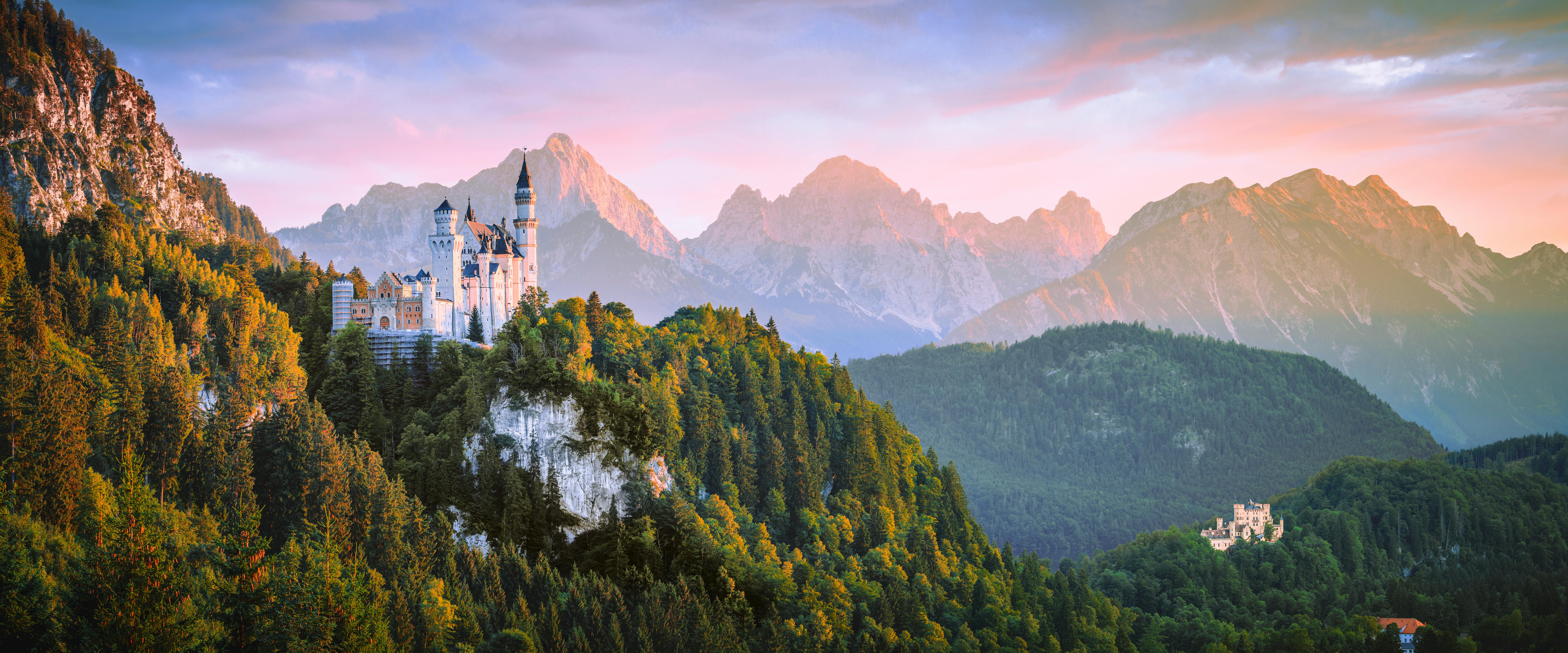 A white castle sits atop a green mountain peak, surrounded by rolling hills, bathed in the golden light of sunset, a stunning sight. - free wallpaper image