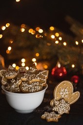 A white bowl filled with gingerbread cookies decorated with white frosting, with some scattered around it, the background is blurred lights and a Christmas tree. - wallpaper image