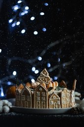 A gingerbread house cake decorated with icing and candy, with scattered snowflakes and blue lights in the background - wallpaper image