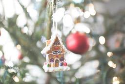 A gingerbread house ornament hangs on a Christmas tree, the ornament is decorated with colorful candies. - wallpaper image