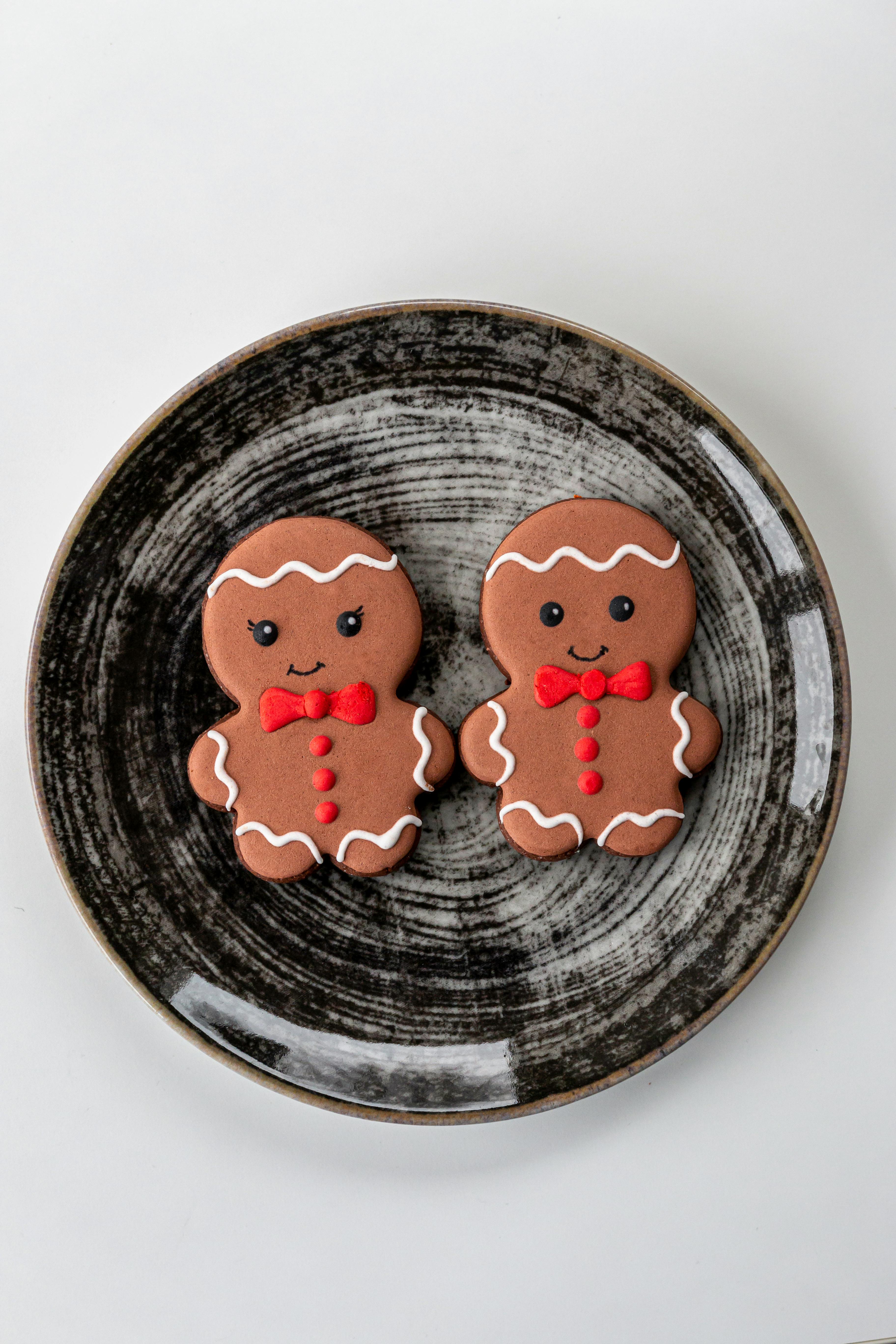 Two gingerbread men decorated with red bow ties on a black plate - wallpaper image