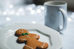 A gingerbread man on a white plate with a cup of water next to it. - wallpaper image