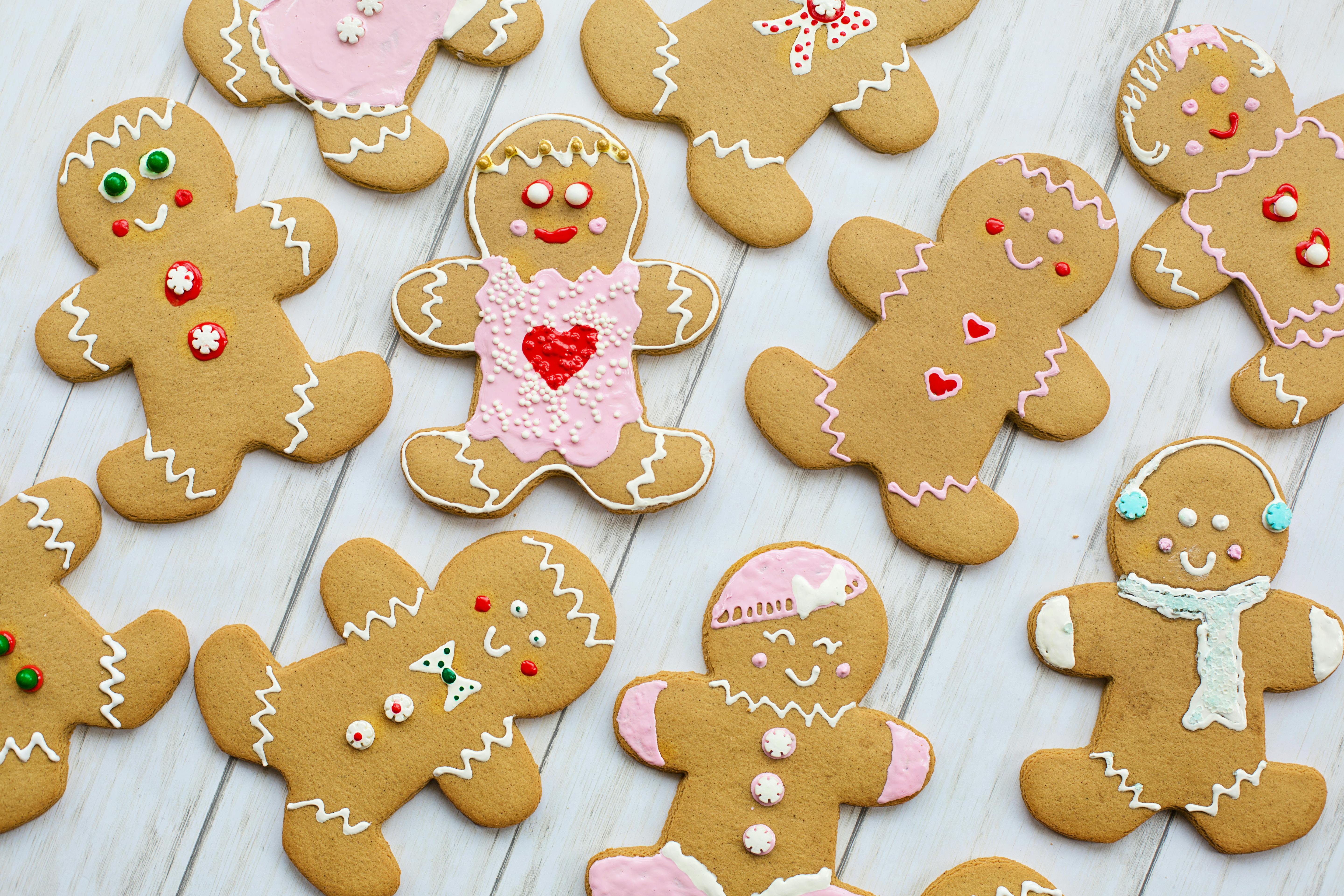 Many gingerbread men are placed together, they are wearing different decorations, the background is a white wooden board. - wallpaper image