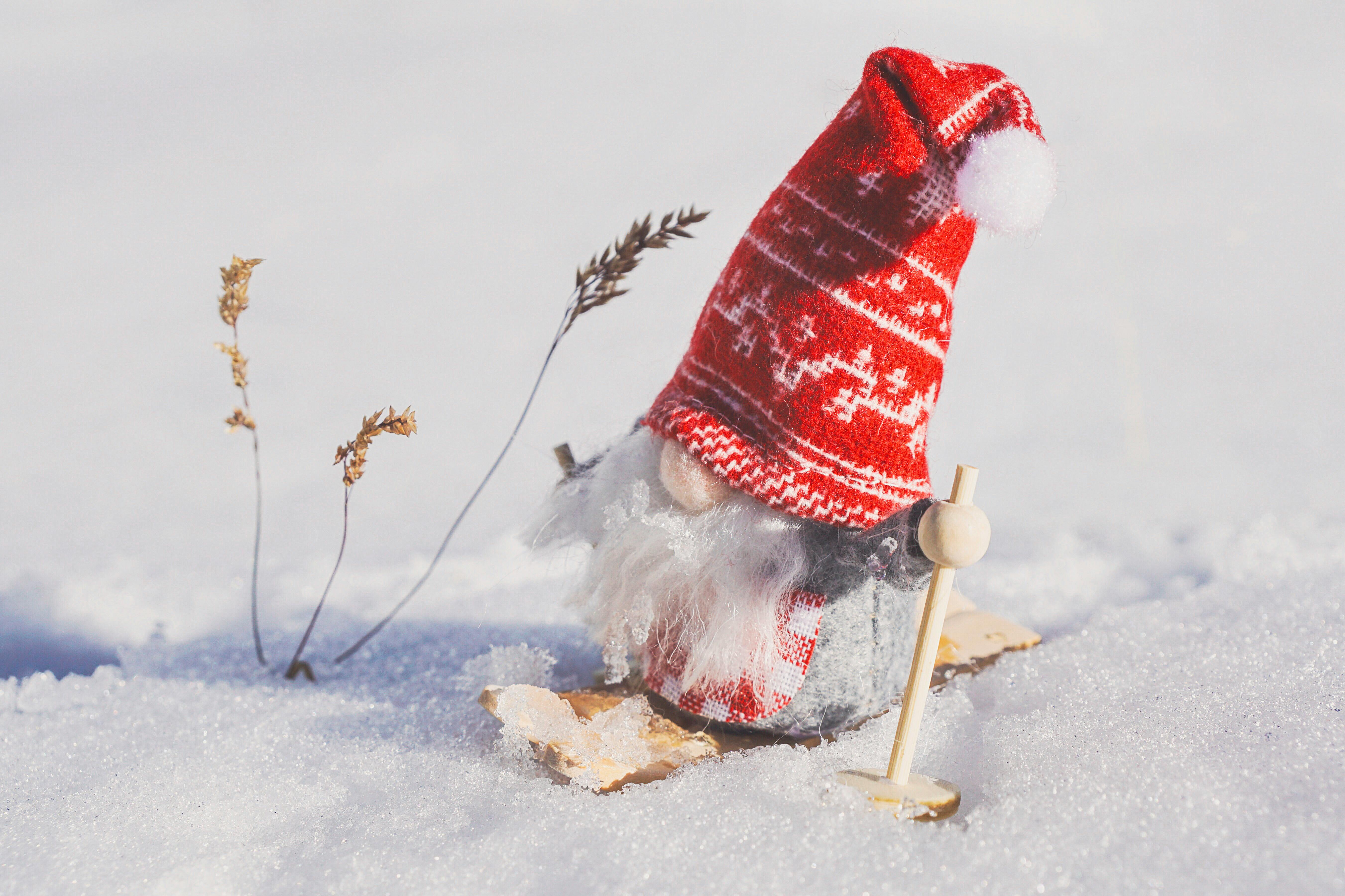 A gnome wearing a red hat and sweater is playing with skis. - wallpaper image