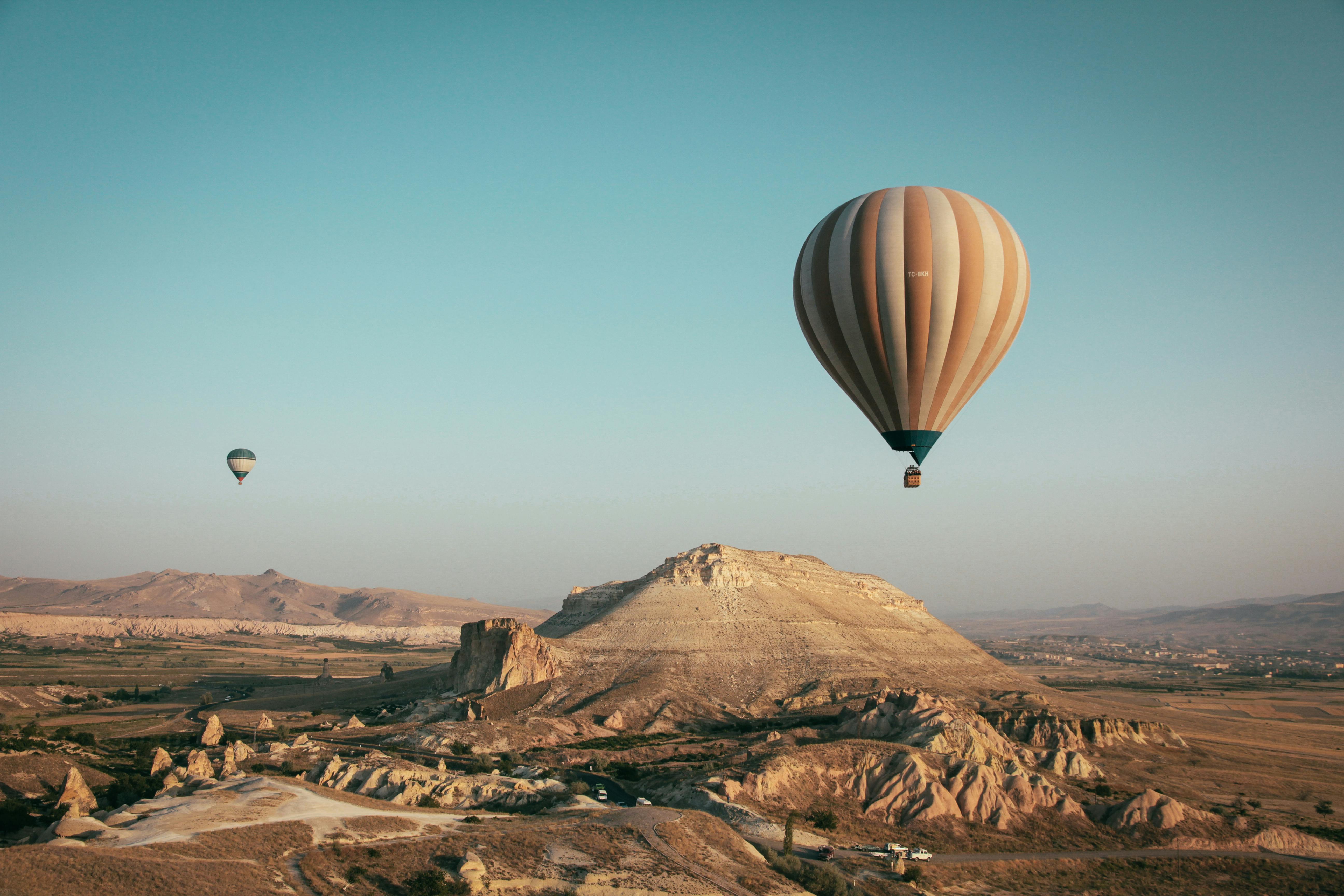 Two hot air balloons fly under the blue sky and white clouds, and below is a desolate Gobi desert. - free wallpaper image