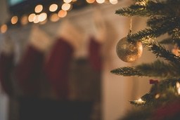 A gold ornament hangs on a Christmas tree with blurry lights and stockings in the background. - wallpaper image