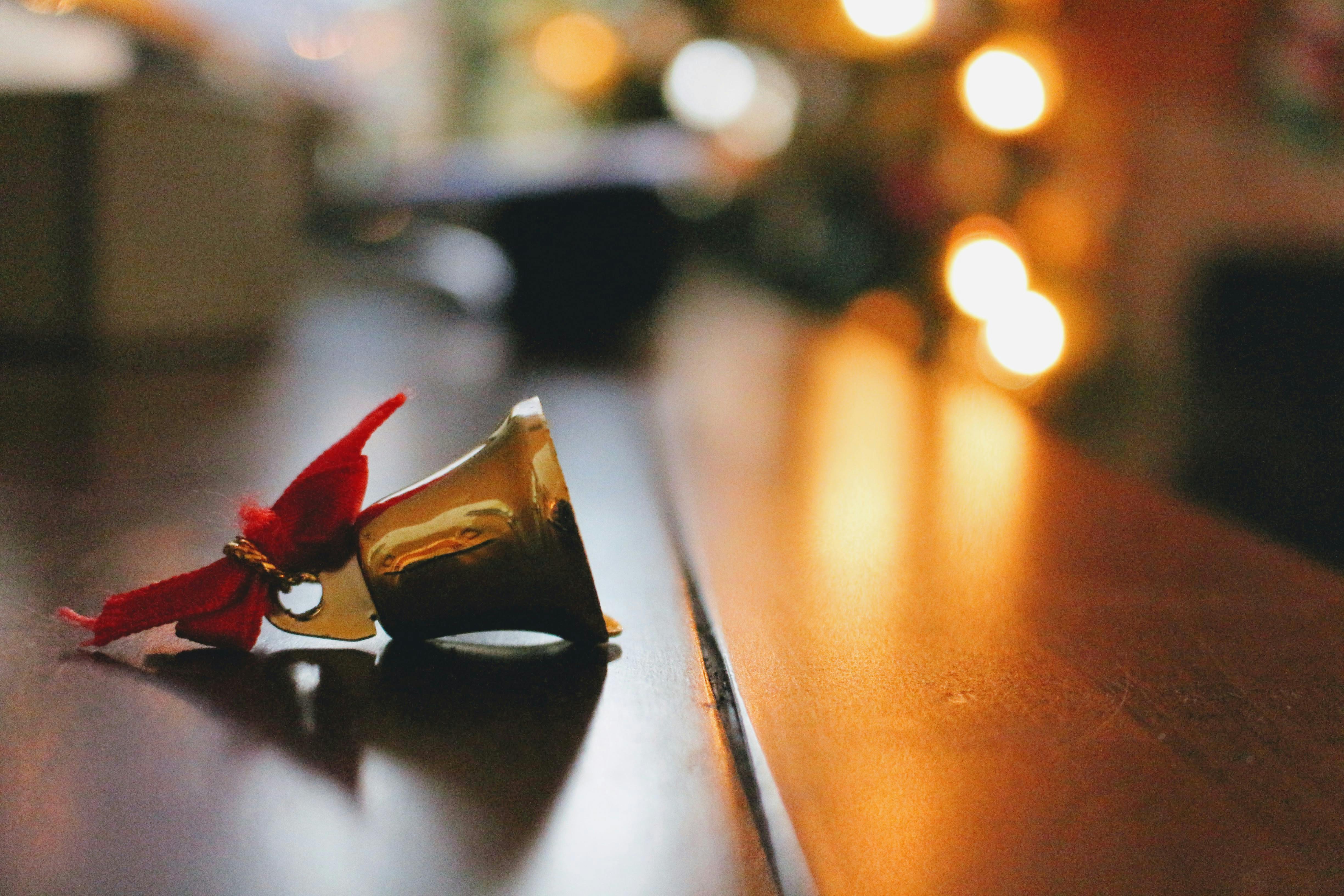 A golden bell with a red ribbon on a wooden table, the background is warm-toned lights. - wallpaper image