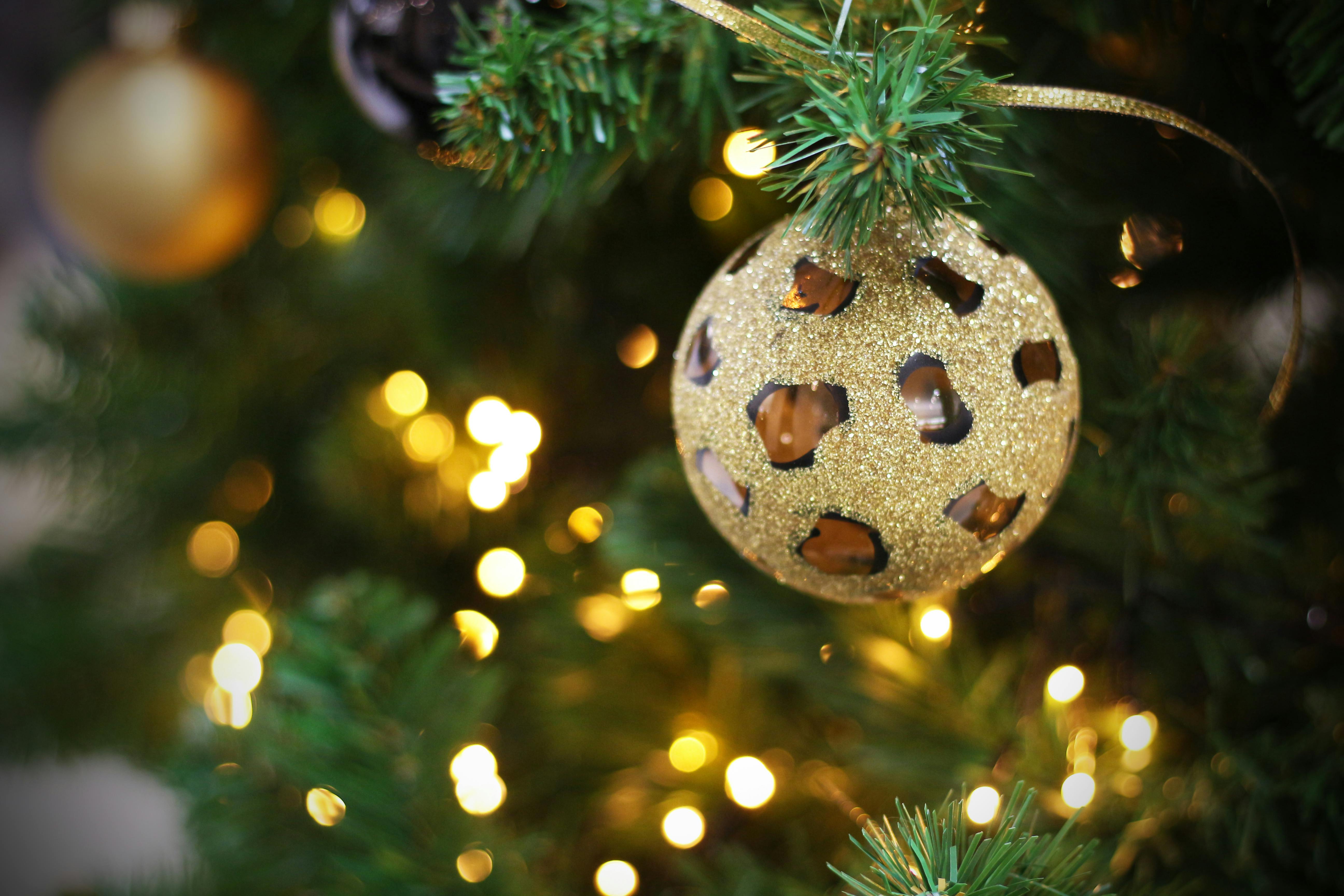 A gold Christmas bauble with a leopard print pattern hangs on a Christmas tree, with green branches and twinkling lights in the background. - wallpaper image