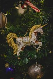 A golden unicorn ornament hangs on a Christmas tree. - wallpaper image