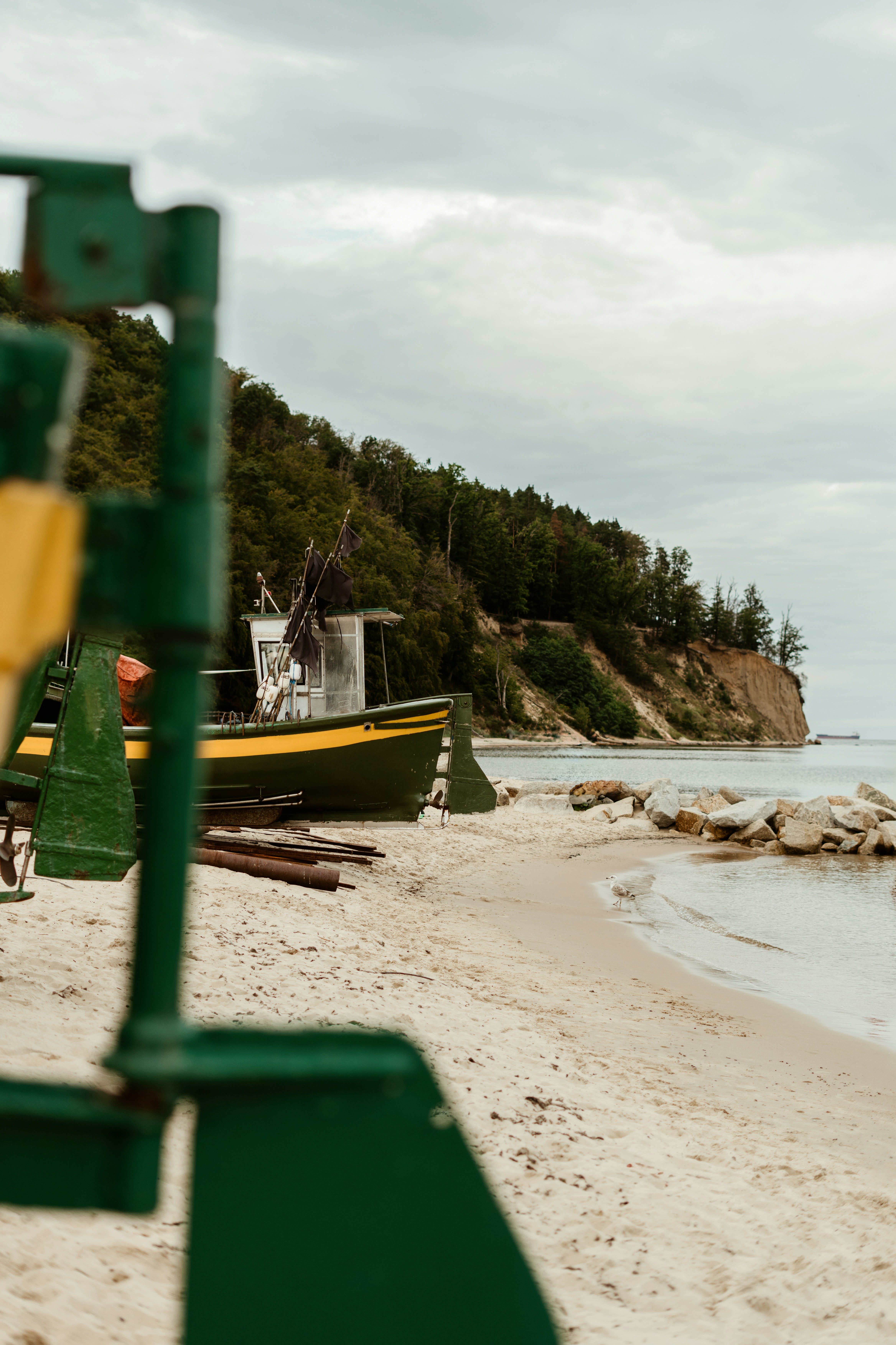 A green boat is anchored on a sandy beach, with green hills on the shore and gray clouds in the sky. - free wallpaper image