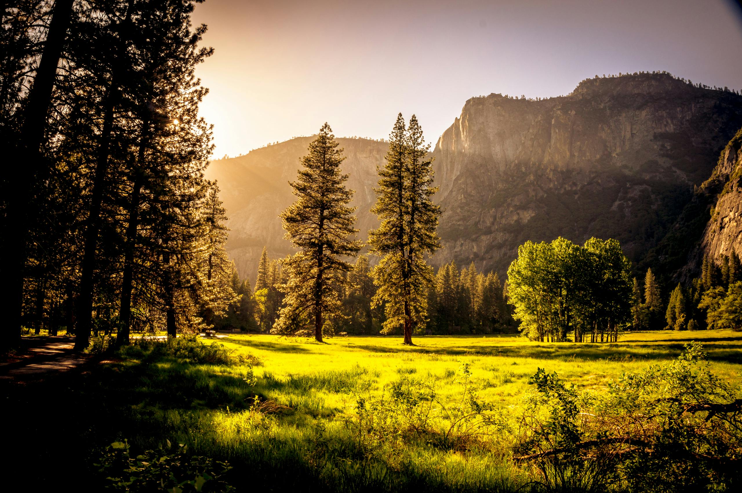 Green grass covers the meadow at the foot of the mountain on a sunny morning, with mist covering the distant peaks. - free wallpaper image