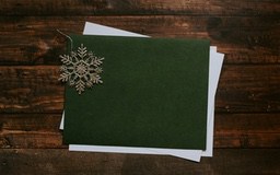 A green paper with a silver snowflake decoration on top, the background is a wooden table. - wallpaper image