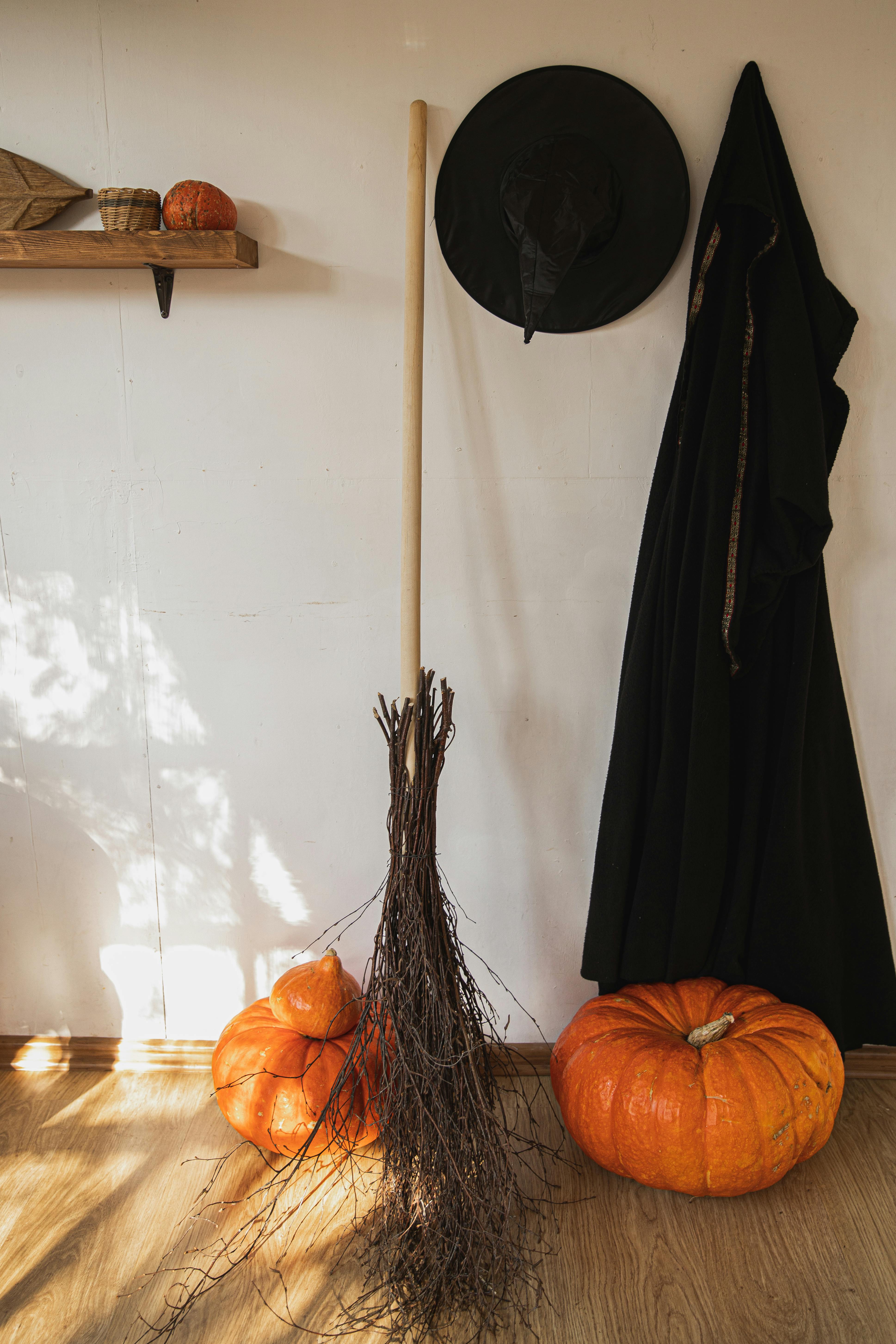 A broom, a witch's hat and a black robe are placed against the wall, with two pumpkins on the floor, creating a Halloween atmosphere. - wallpaper image