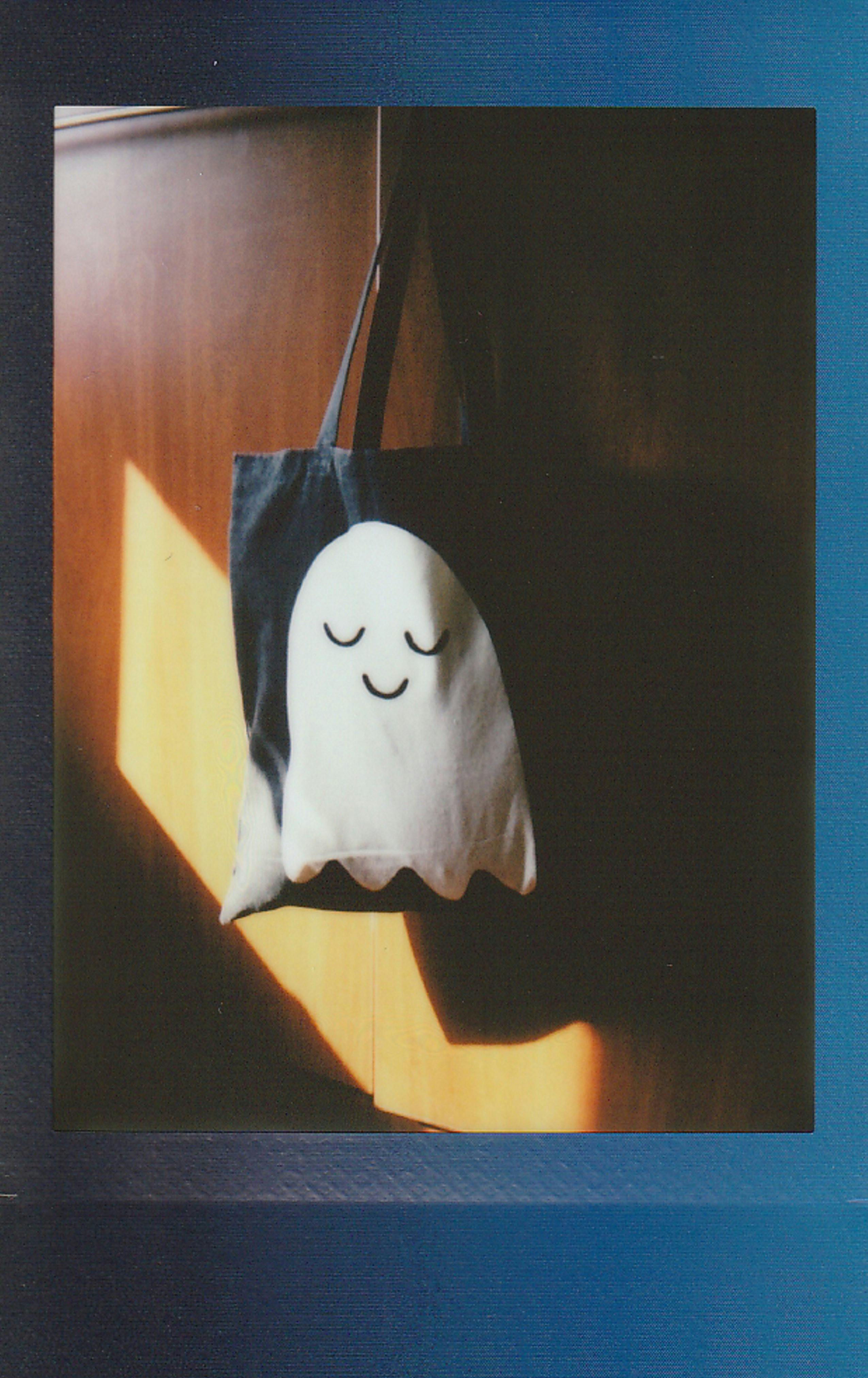 A black canvas bag hangs on a wooden door with a cute little ghost pattern on it. - wallpaper image