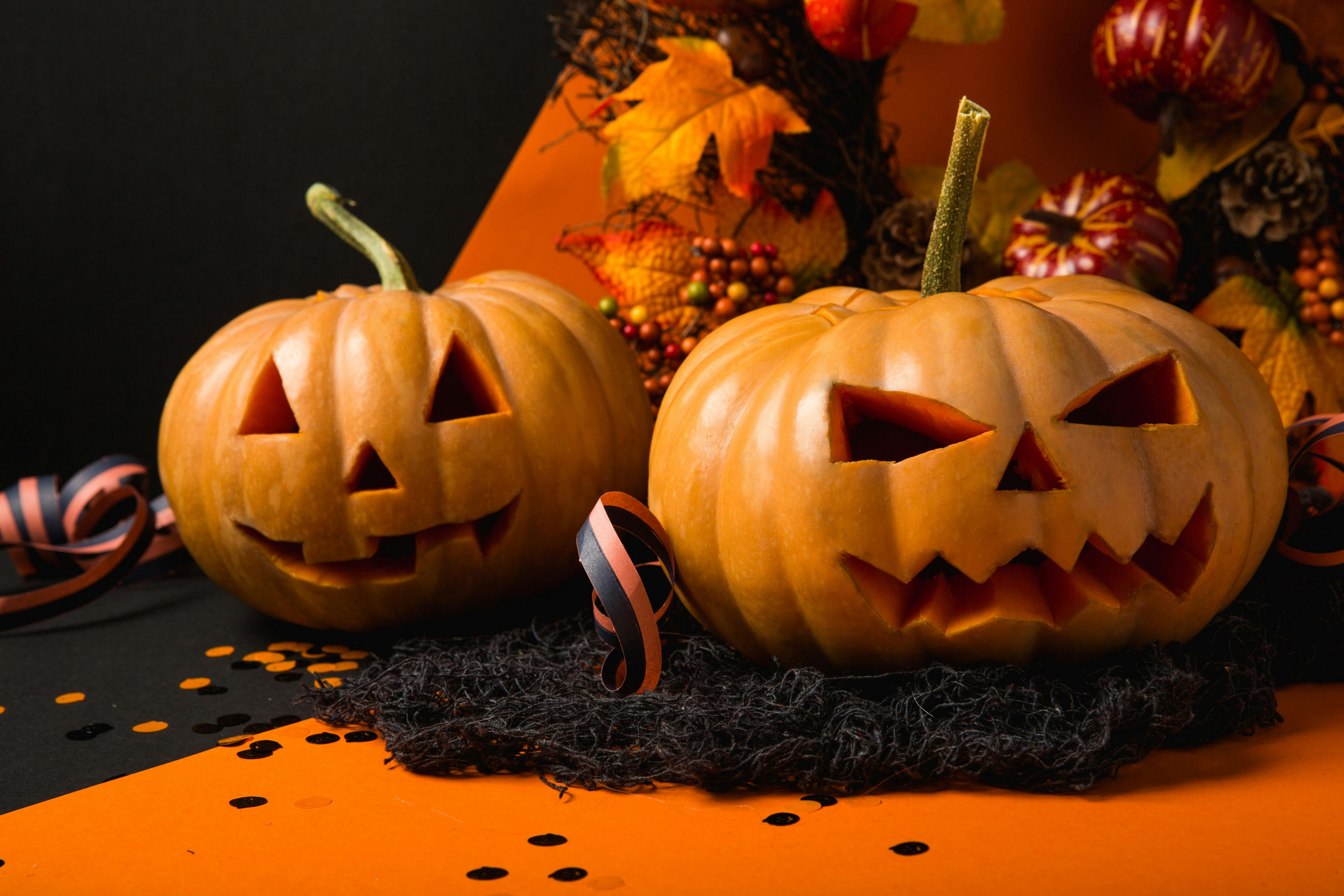 Two jack-o&apos;-lanterns, one friendly and one menacing, are placed against a black and orange background. - wallpaper image