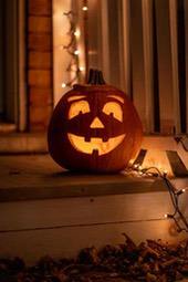 A jack-o&apos;-lantern sits on a porch step, carved with a smiling face, with lights strung around it. - wallpaper image