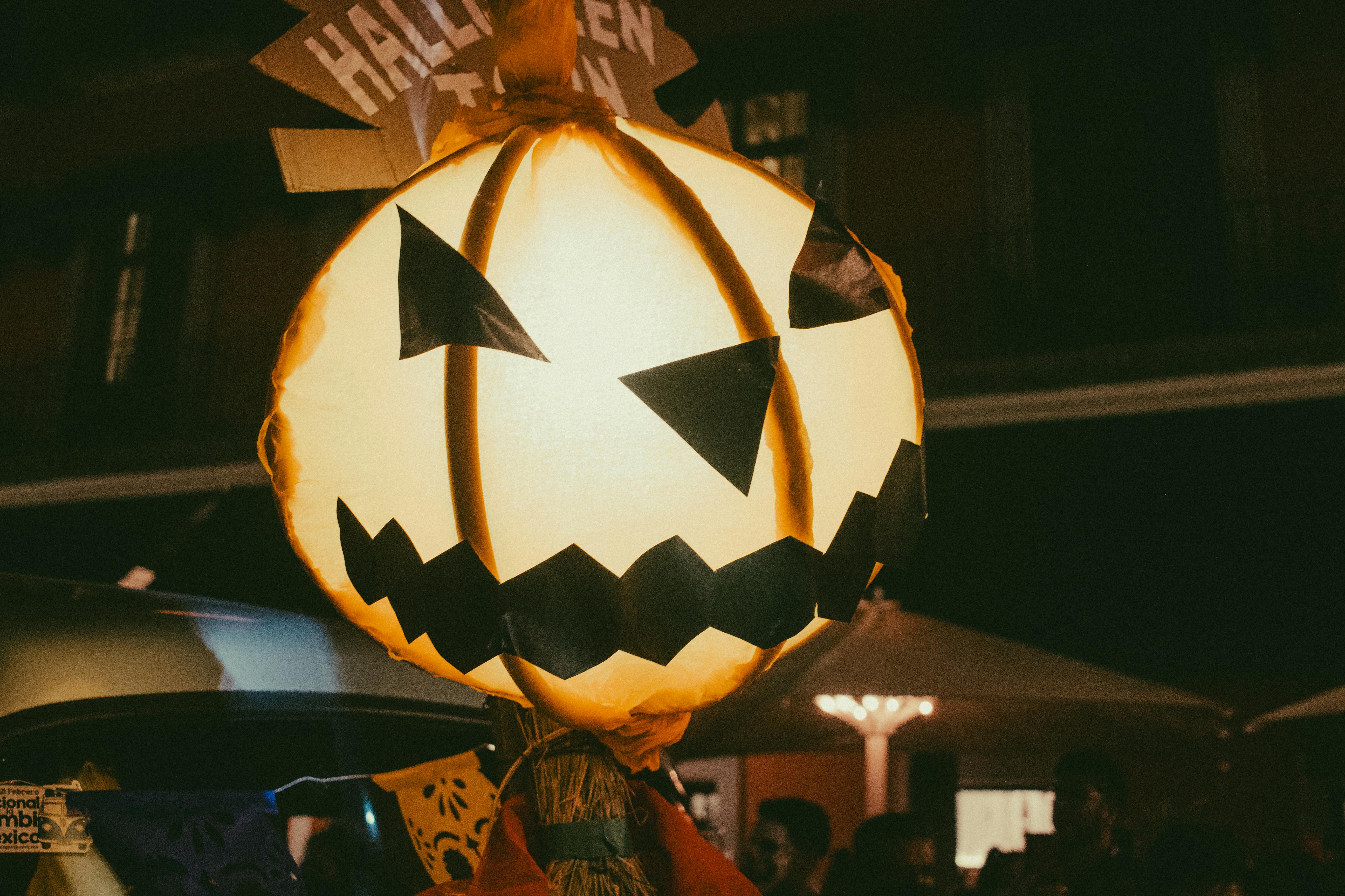 A jack-o&apos;-lantern is held up in the night, its light illuminating the surroundings. - wallpaper image