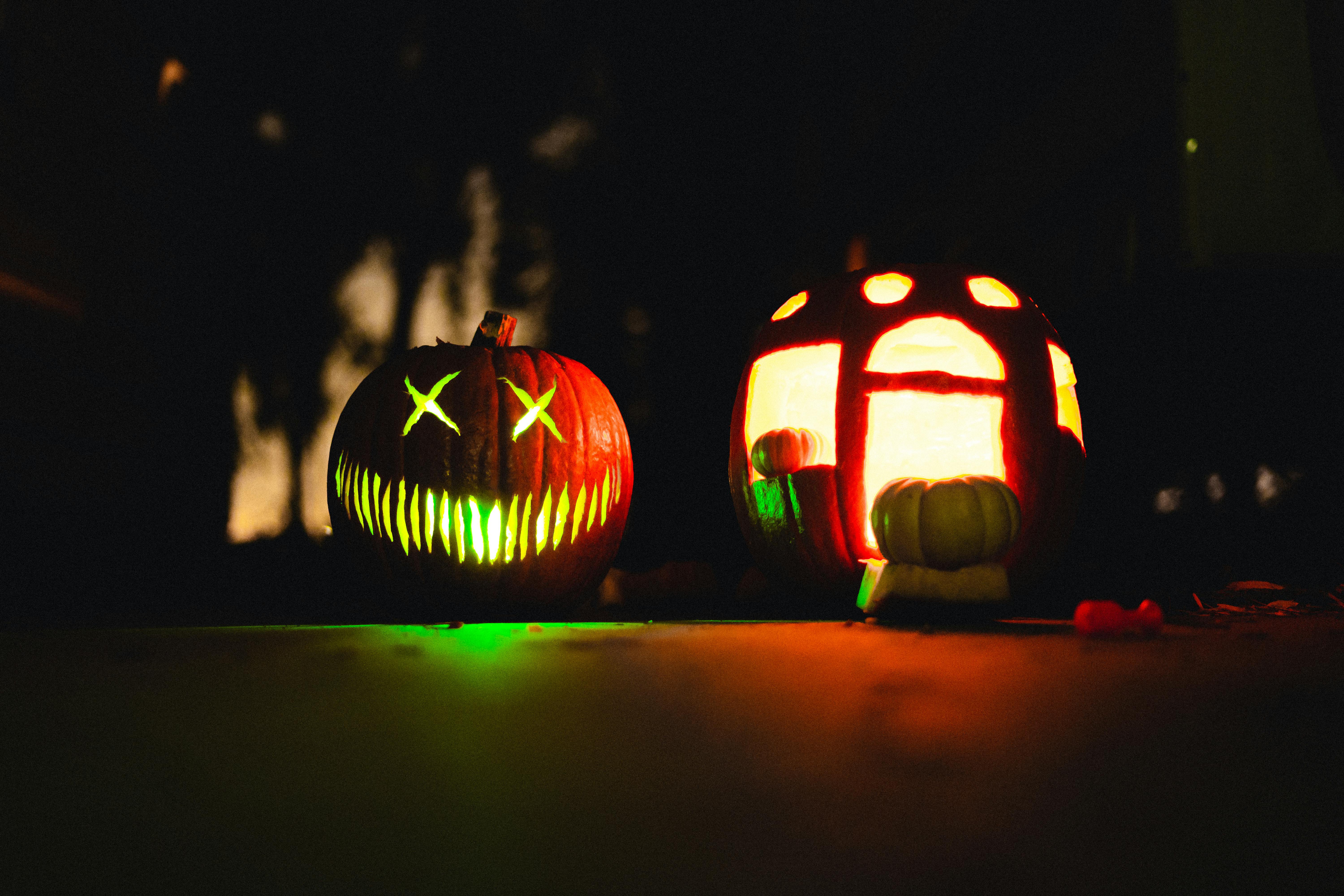 Two jack-o'-lanterns, one carved into a smiling face and the other into a house, emit a warm glow in the darkness. - wallpaper image