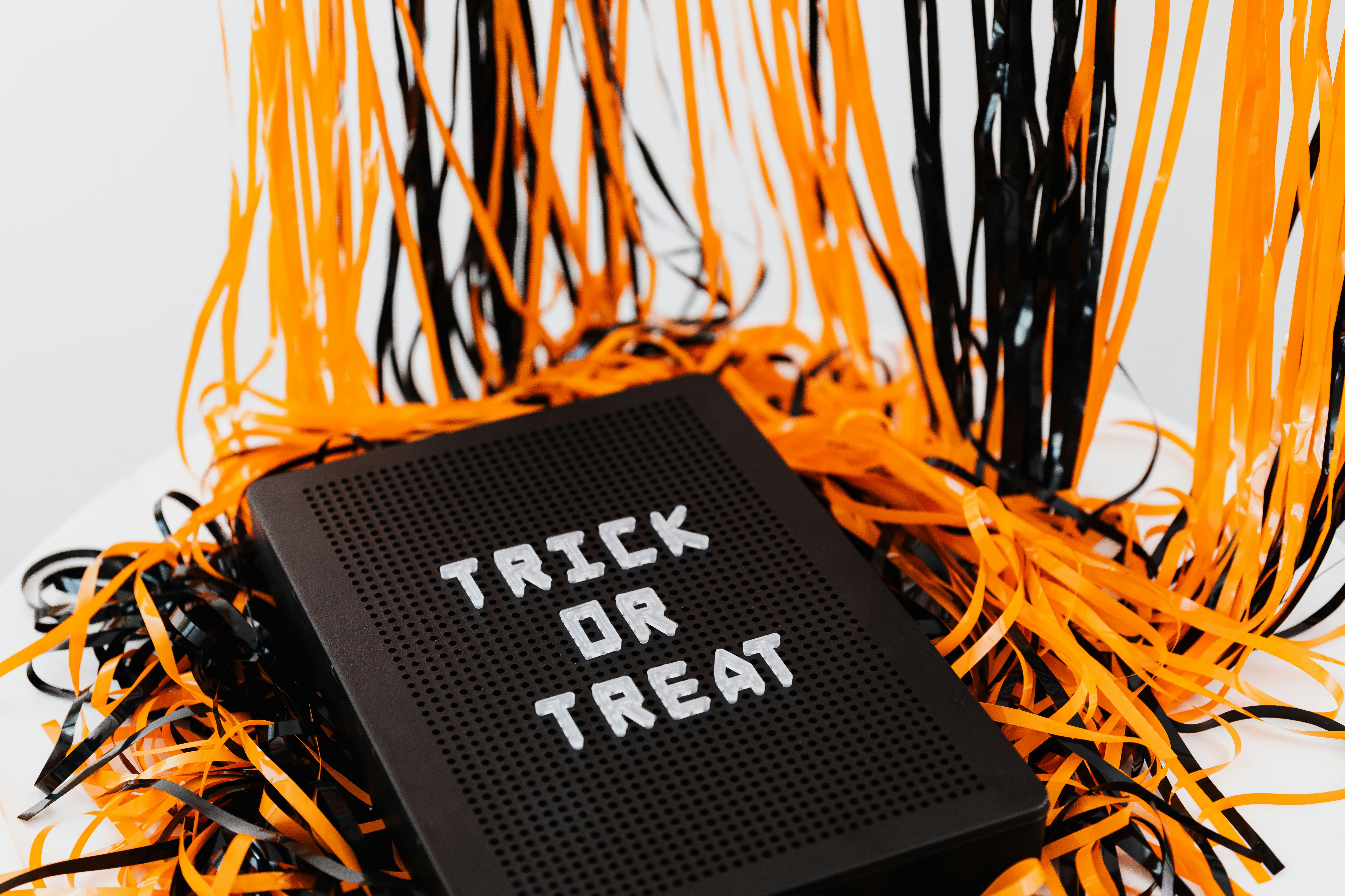 A black letter board with the words "trick or treat" on it, surrounded by orange and black streamers. - wallpaper image