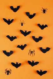 Black paper bats and spiders cutouts on an orange background, creating a Halloween atmosphere. - wallpaper image