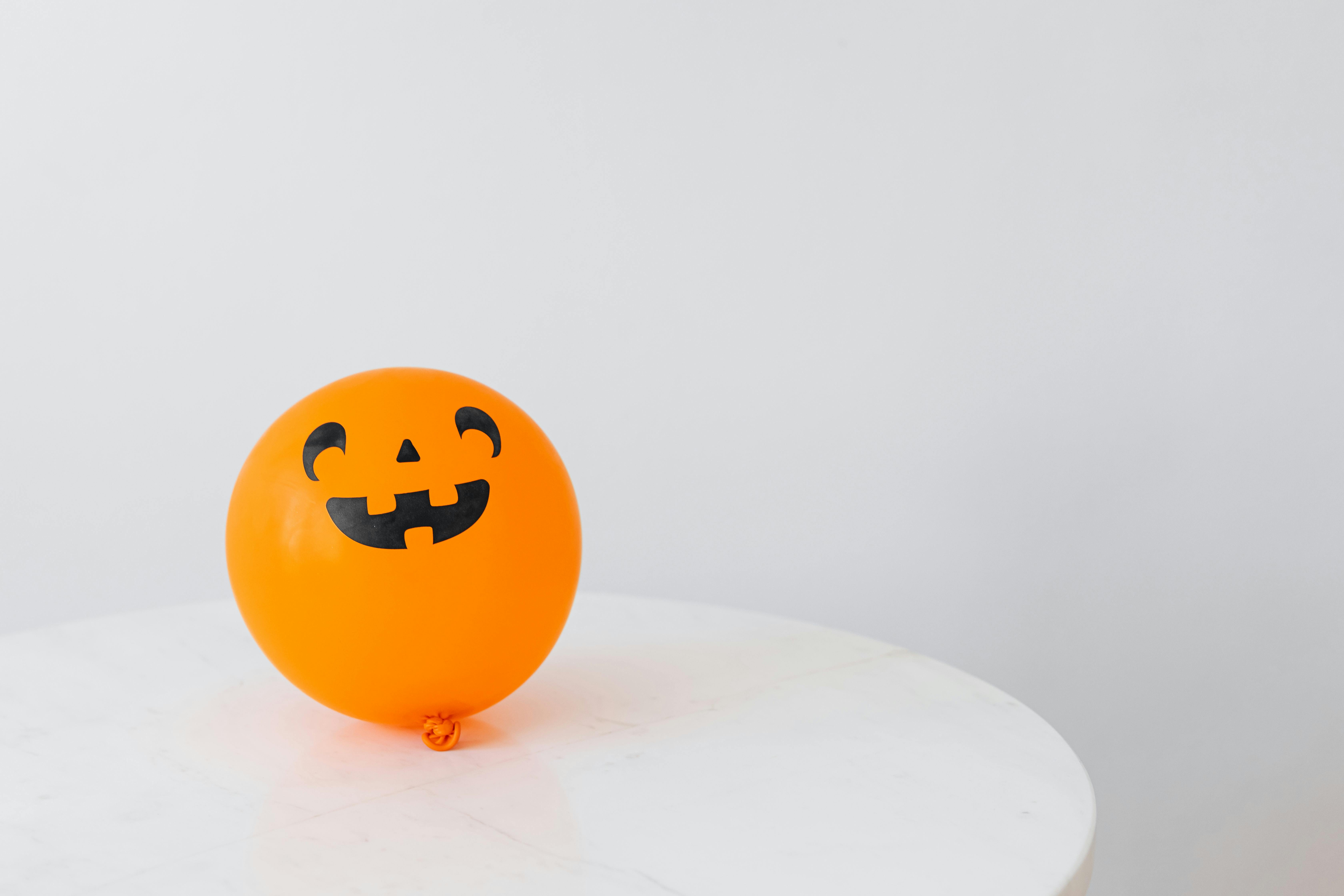 An orange balloon with a pumpkin face on it, placed on a white table. - wallpaper image