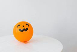 An orange balloon with a pumpkin face on it, placed on a white table. - wallpaper image