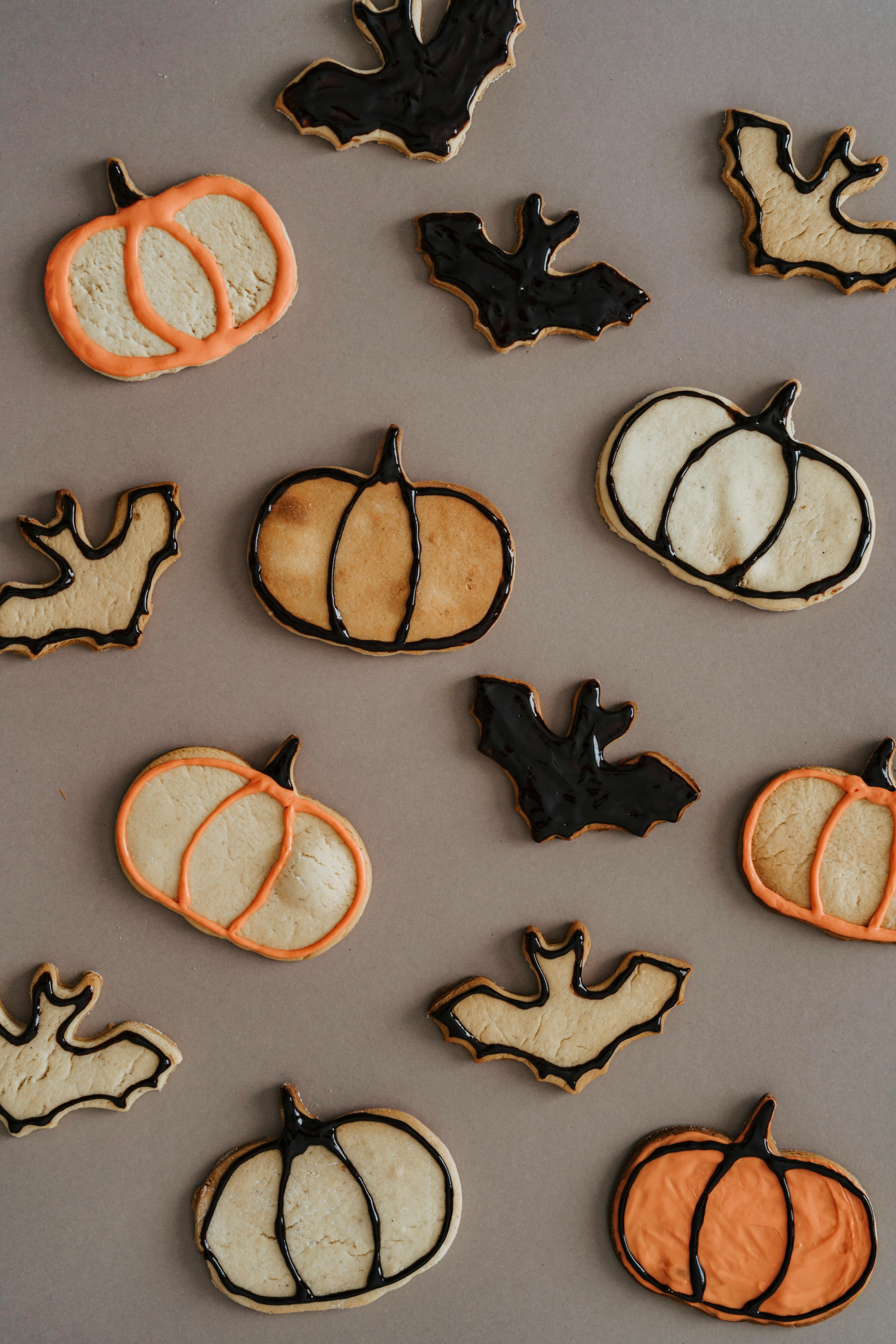 There are some Halloween themed cookies on the table, there are pumpkin shaped and bat shaped ones. - wallpaper image