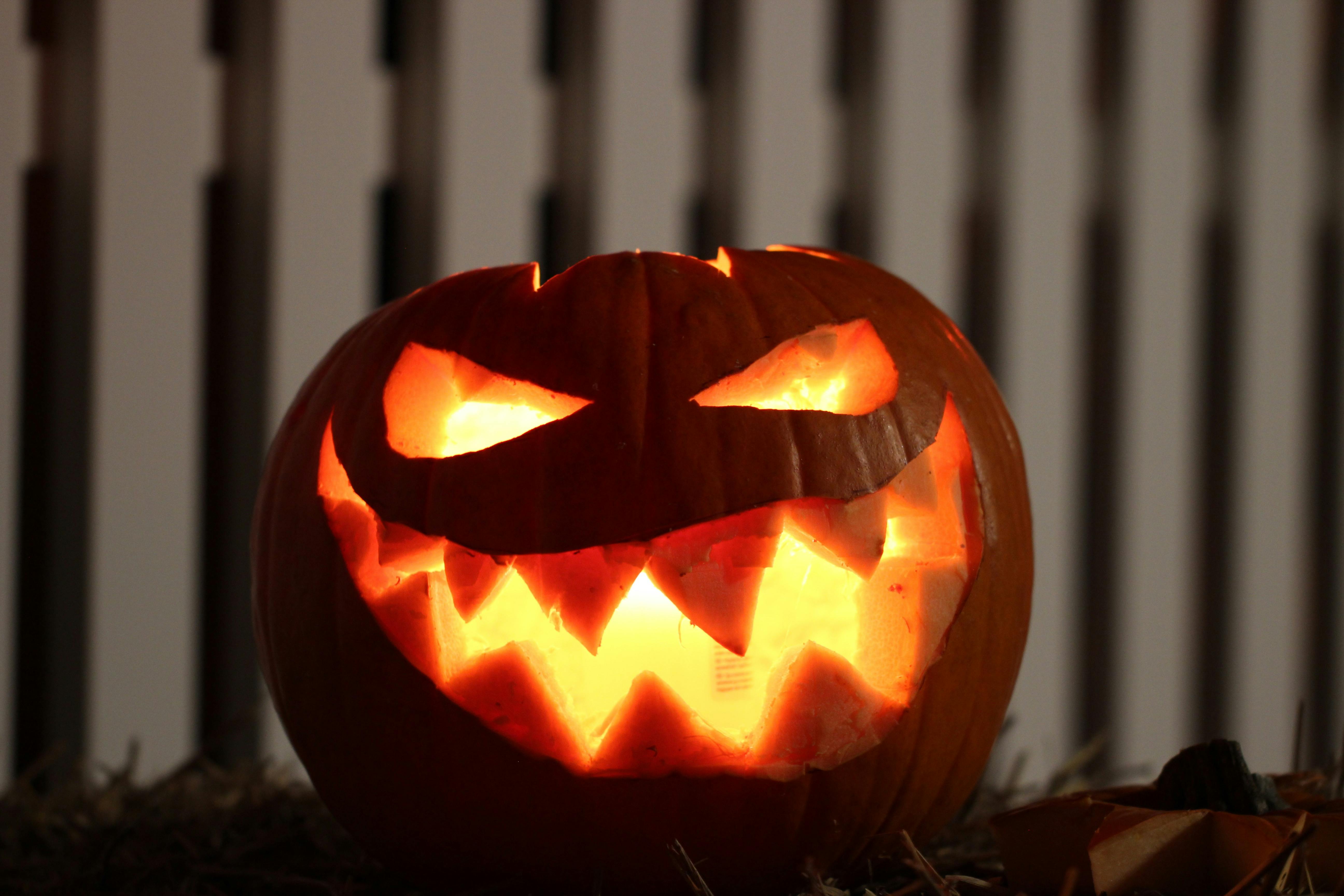 A pumpkin carved into a spooky face with a candle lit inside, emitting an orange glow. - wallpaper image