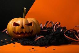 A pumpkin carved with a spooky face, next to a black mesh and orange and black ribbons. - wallpaper image