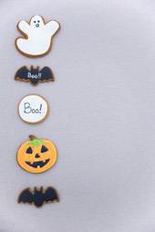 There are several Halloween themed cookies arranged on a gray background, including a ghost, bat, pumpkin and "boo" cookies. - wallpaper image