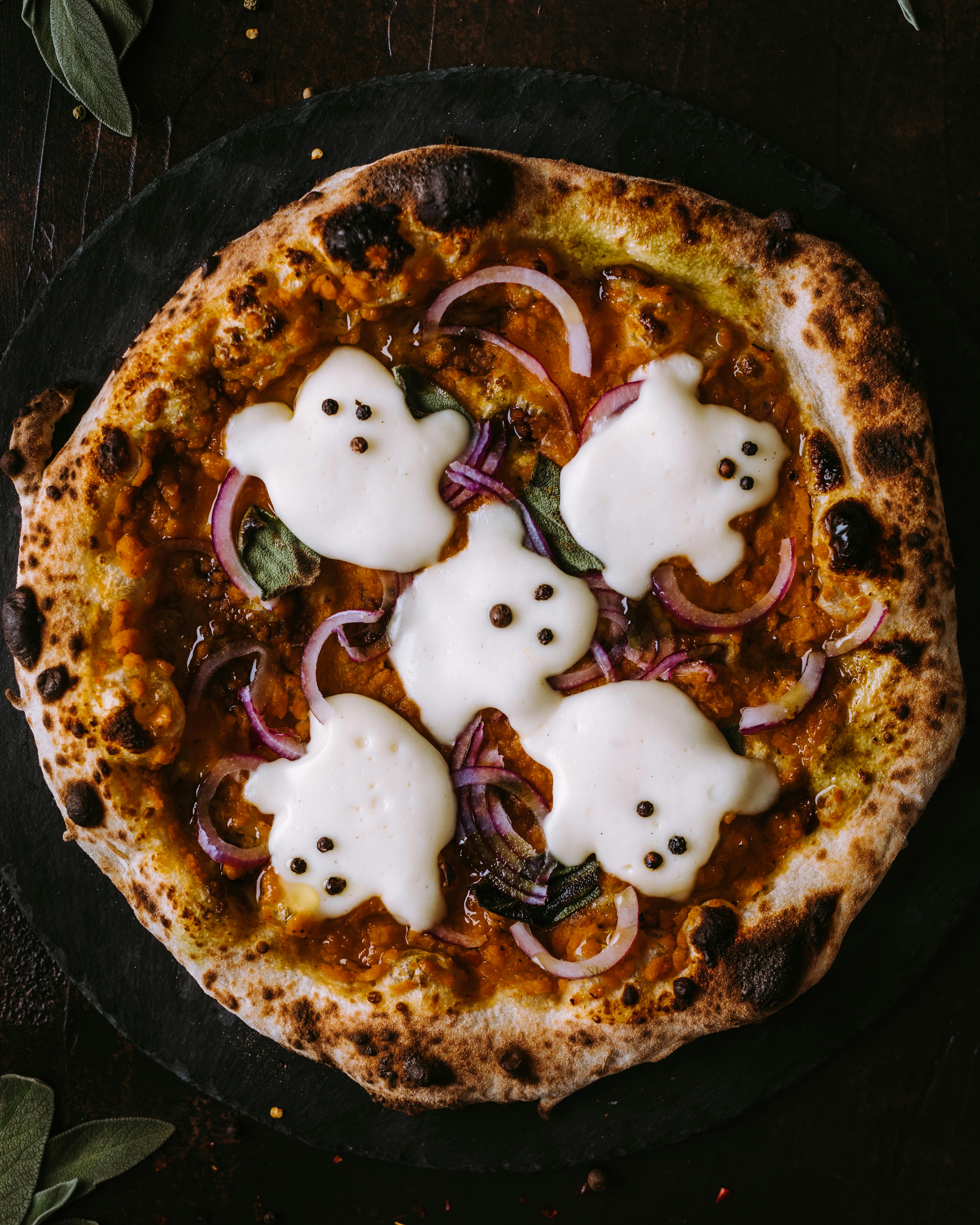 A pizza topped with four ghost shapes made of cheese, surrounded by red onions and pumpkin sauce, looks delicious. - wallpaper image