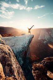 A man is doing a handstand on the edge of a cliff, with a majestic mountain range and sky in the background. - free wallpaper image