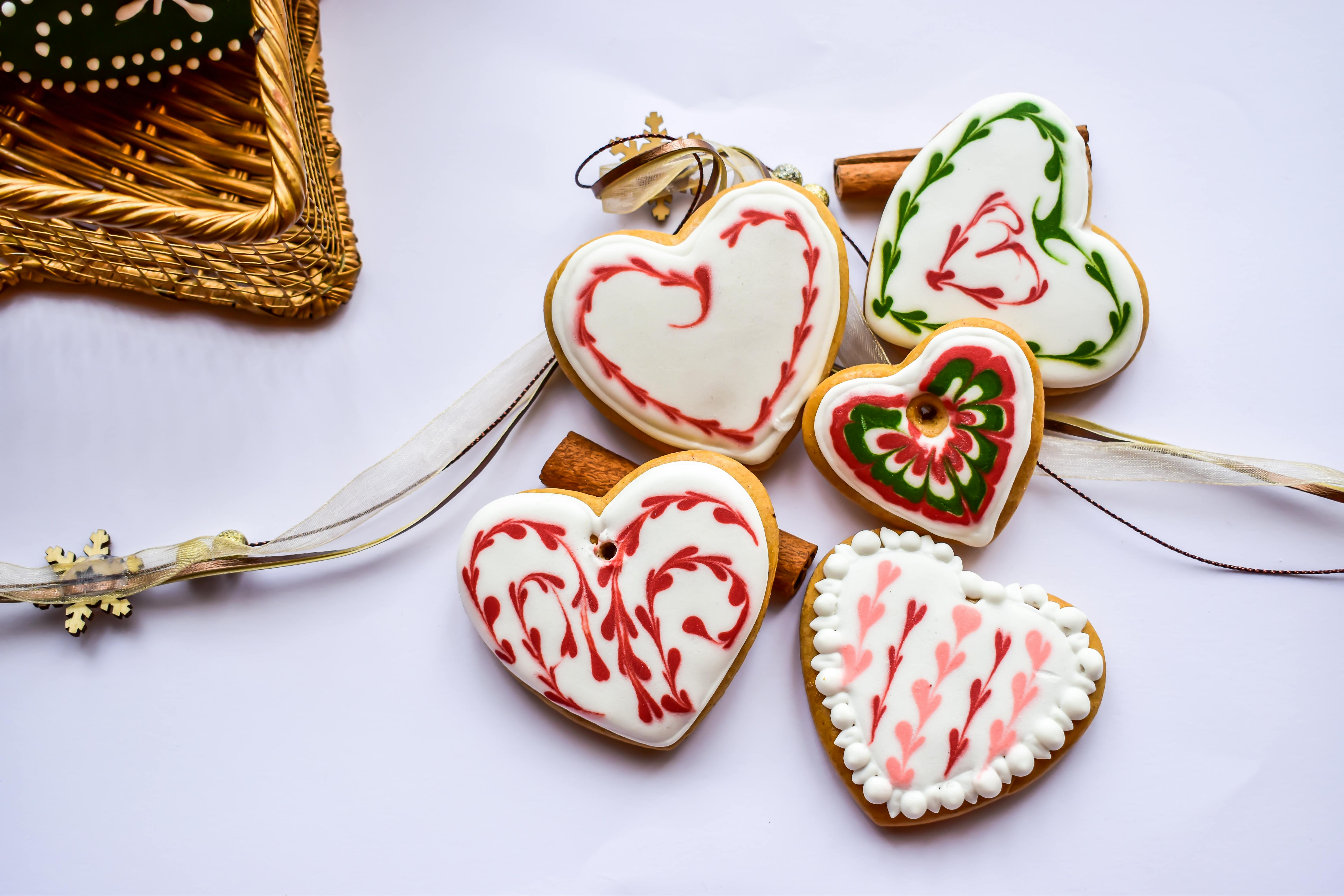 Five heart-shaped gingerbread cookies are decorated with beautiful floral patterns and covered with white frosting, scattered on a white background. - wallpaper image