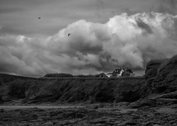 A house built on the edge of a cliff, the sky is full of dark clouds, and two birds are flying in the distance. - free wallpaper image