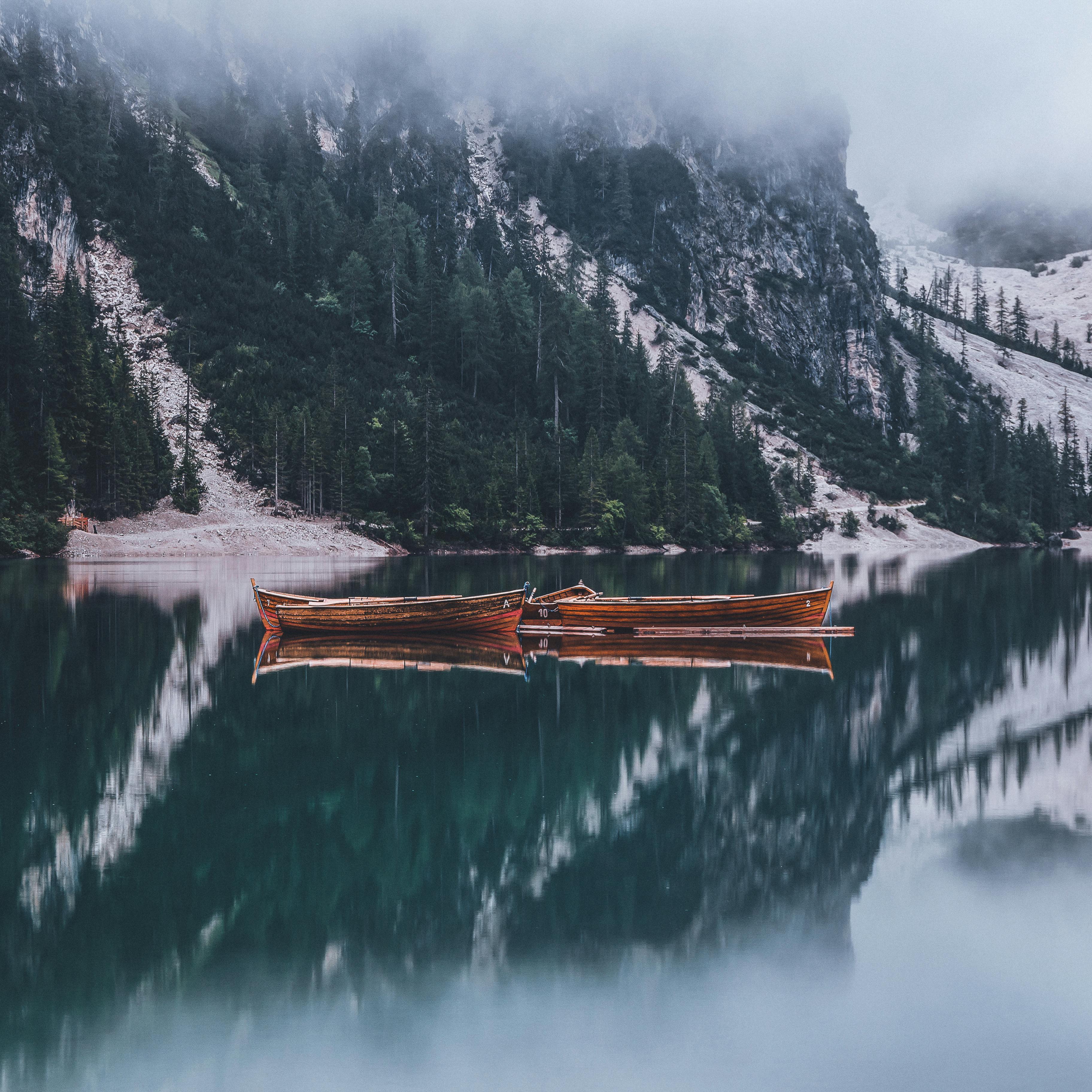 Two wooden boats are moored on a calm lake, the lake water reflects the surrounding mountains and trees, and the distant mountains are shrouded in mist. - free wallpaper image