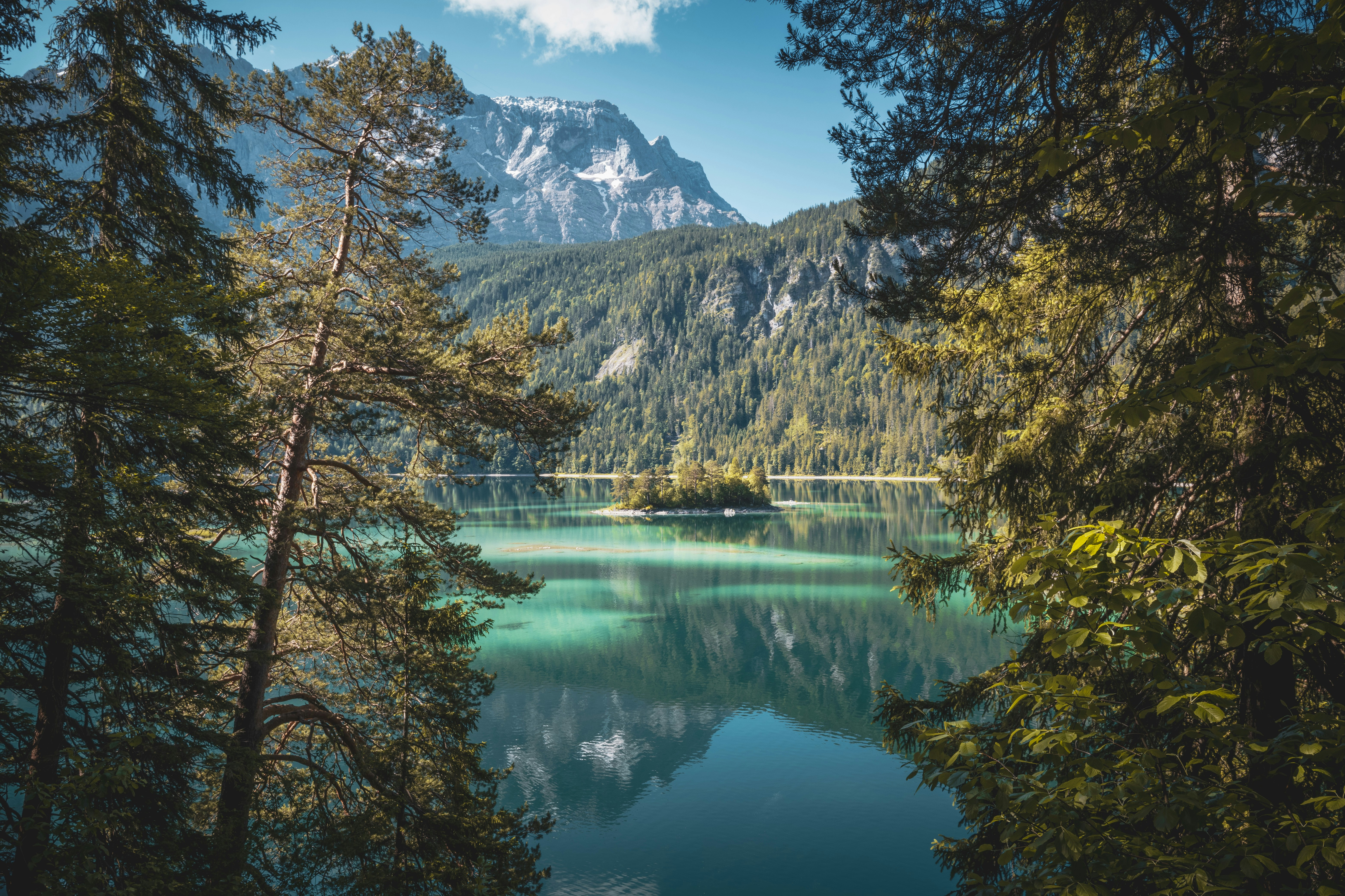 A picturesque lake with clear water reflecting the surrounding snow-capped mountains and forest, a small island in the center of the lake, the scenery is peaceful and beautiful. - free wallpaper image