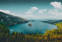 A lake surrounded by green trees, the lake water is clear and calm, with white clouds floating in the sky. - free wallpaper image