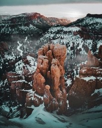 A red rock pillar on a snowy mountain, the top of the mountain is covered with snow, the clouds are swirling, and the scenery is magnificent. - free wallpaper image