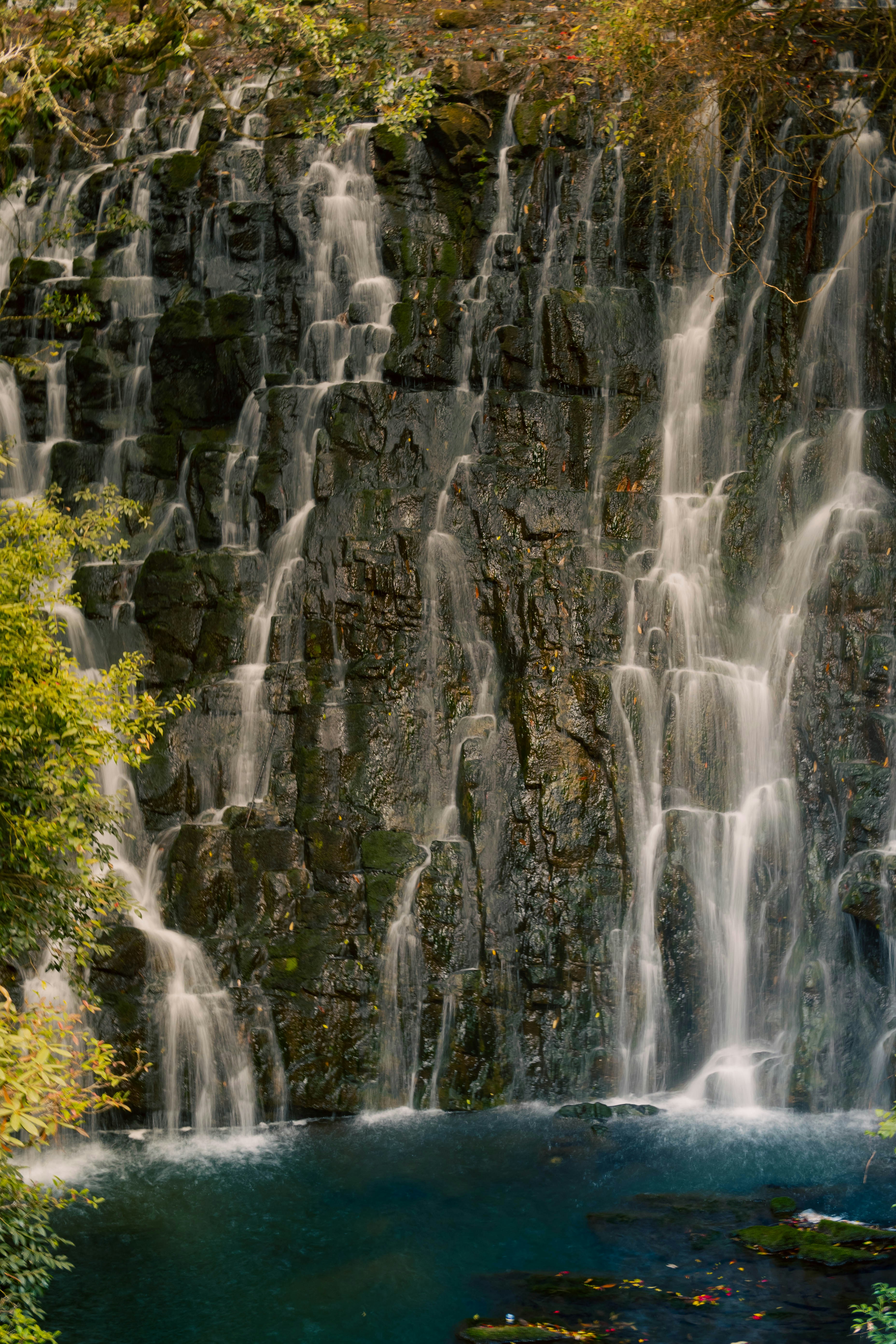 A tall waterfall cascades down a rocky cliff, forming a clear blue pool. - free wallpaper image