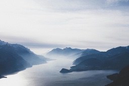 A winding river flows through the misty mountains, the distant peaks are shrouded in fog. - free wallpaper image