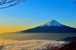 Mount Fuji is covered in snow at the top, with a sea of clouds surrounding the peak. The distant sky is a gradient of blue and yellow. - free wallpaper image