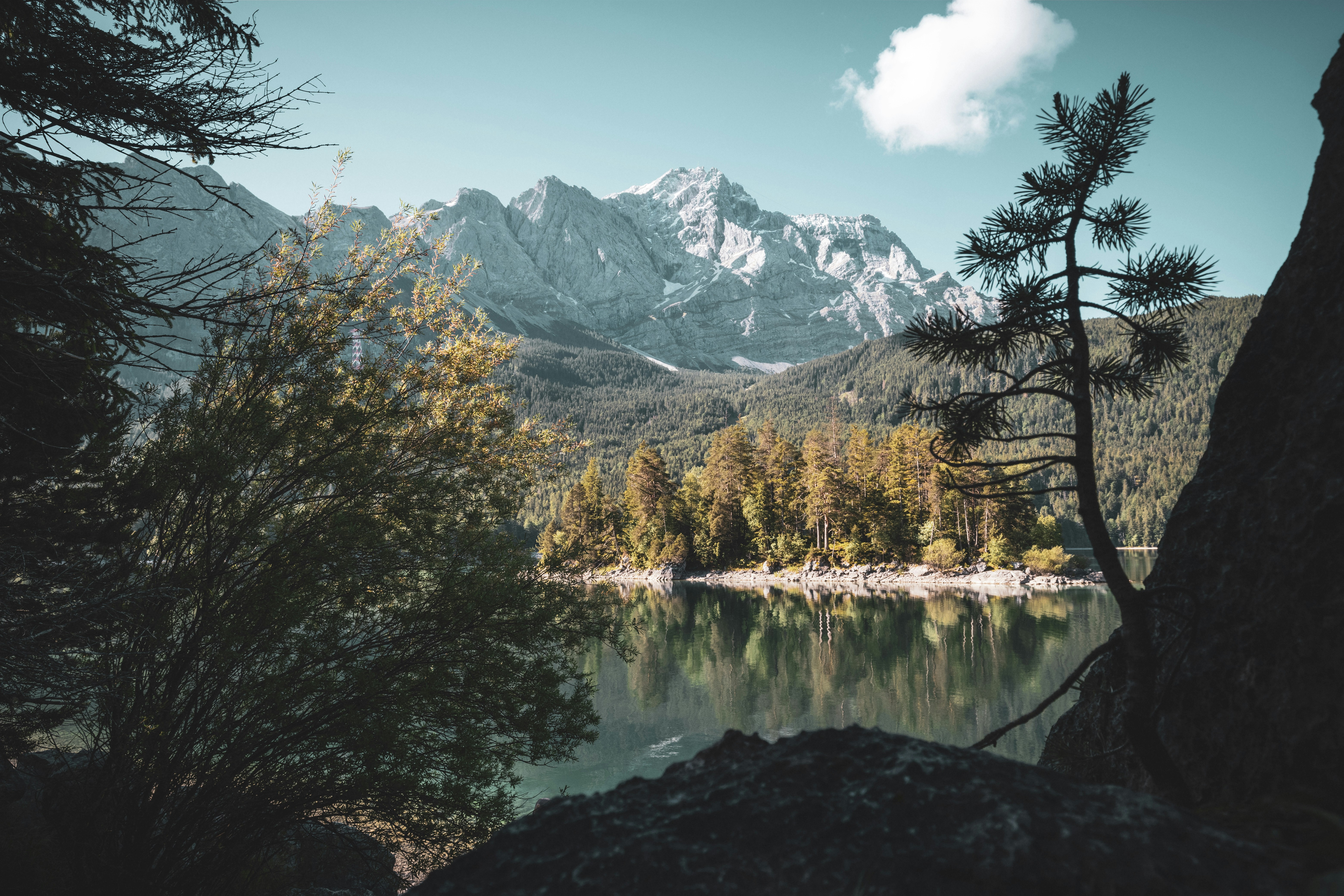 A mountain lake with clear water reflecting the blue sky, white clouds and distant snow-capped mountains. - free wallpaper image