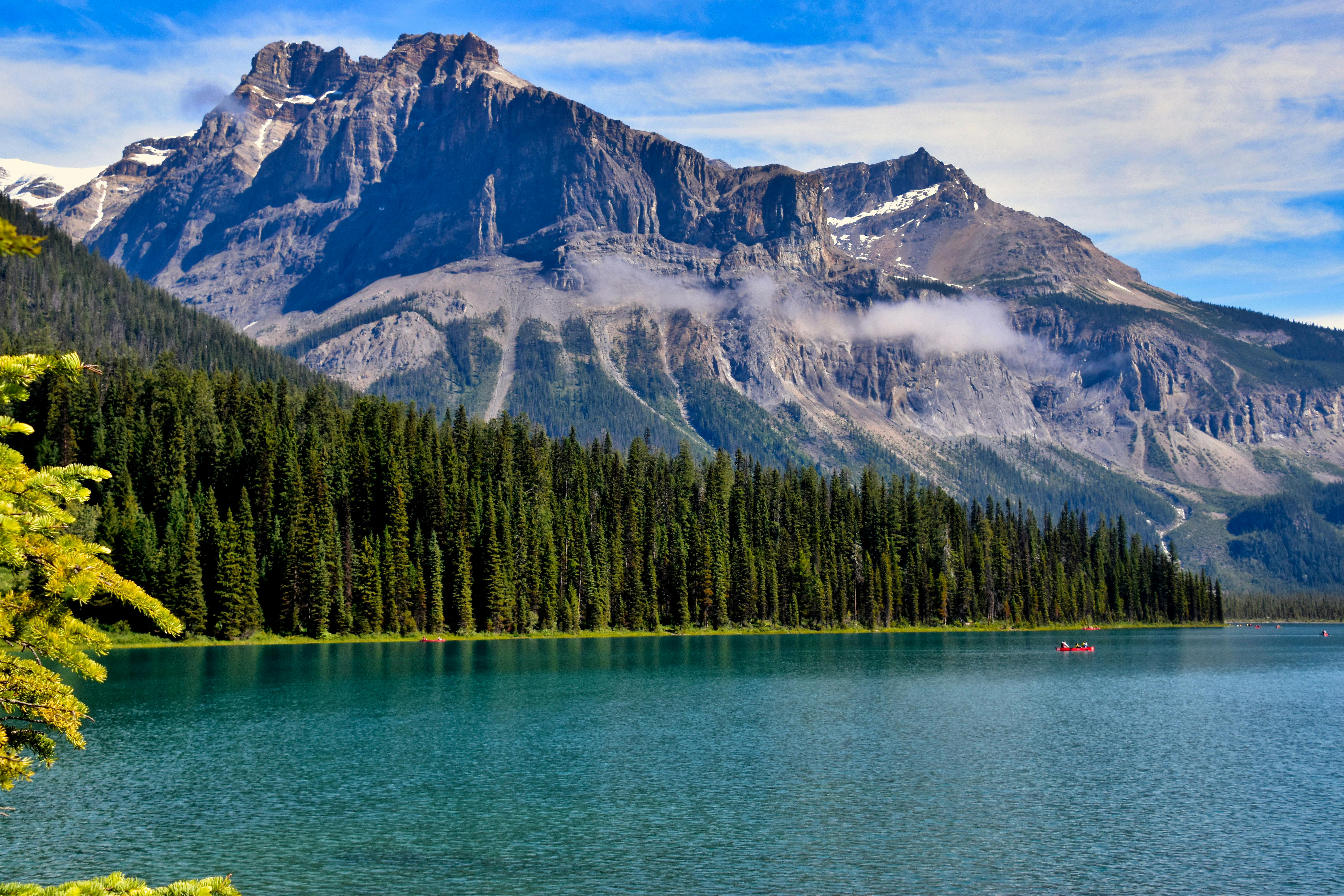 A row of towering peaks reflected in the azure lake, with dense forests on the shore and a few small boats quietly moored on the lake. - free wallpaper image