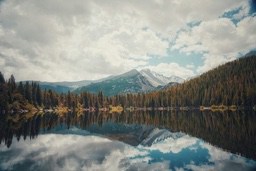 A mountain lake with clear water reflecting the sky and clouds, surrounded by dense forest. - free wallpaper image